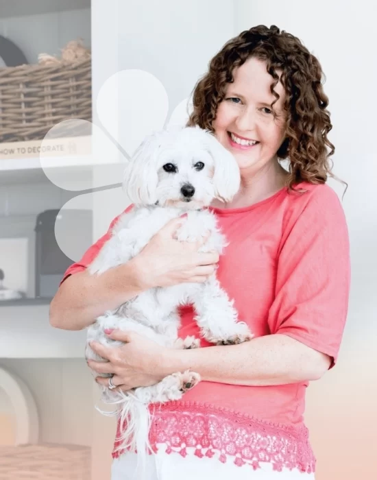 Kate Hatherell holding her fluffy white dog in her living room